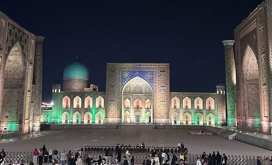 Illuminated historic Registan square in Samarkand at night with crowds gathered in the plaza.
